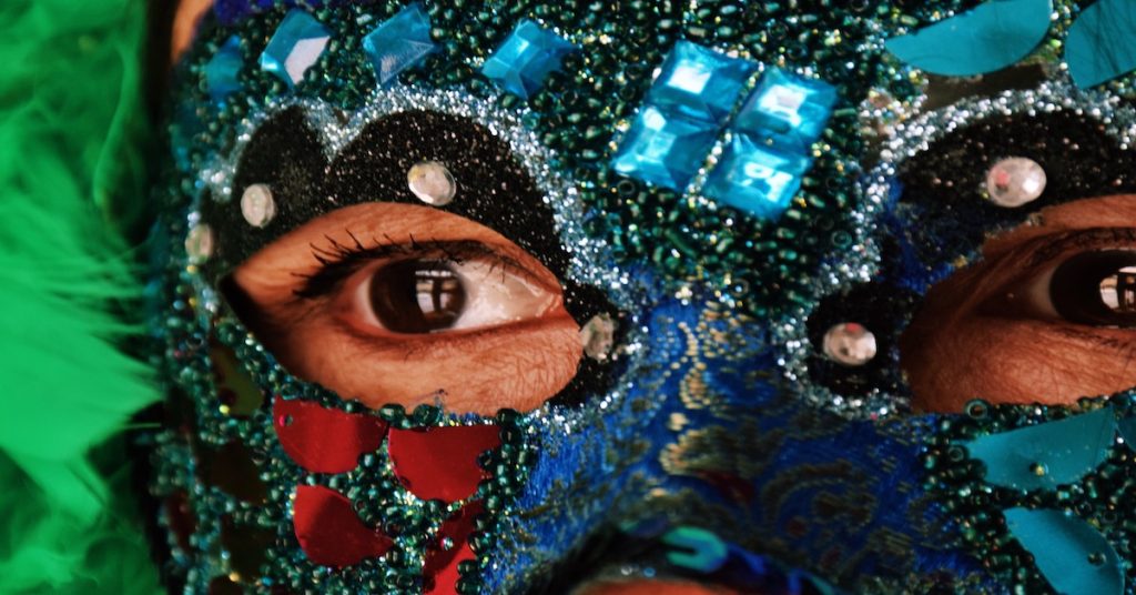 mujer con máscara de cristales, brillos y plumas durante un desfile de carnaval